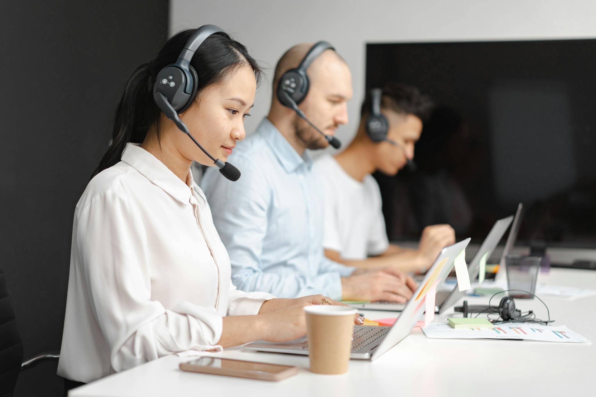Home 10 Customer service agents efficiently handle calls using laptops and headsets in a modern office.